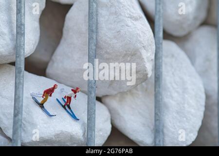 Die Miniaturfiguren als Skifahrer, die auf Skiern auf dem weißen Stein abfahren Stockfoto