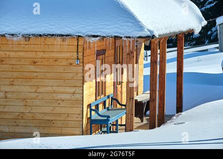 Kleines Holzhaus mit frischem Schnee bedeckt, umgeben von hohen Pinien in den Winterbergen. Stockfoto