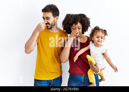 Junge Familie aus schwarzer Mutter und hispanischer Vater mit Tochter, die etwas stinkendes und ekelhaftes riecht, einen unerträglichen Geruch hat und den Atem anhält Stockfoto