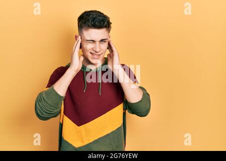 Junge kaukasische Junge mit Ohren Erweiterung tragen lässige Sweatshirt bedeckt Ohren mit Fingern mit verärgerten Ausdruck für den Lärm der lauten Musik. Taub Stockfoto