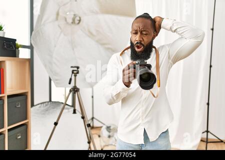 afroamerikanischer Fotograf Mann, der im Fotostudio arbeitet, ist verrückt und verängstigt mit Händen auf dem Kopf, ängstlich und überrascht von Schock mit offenem Mund Stockfoto