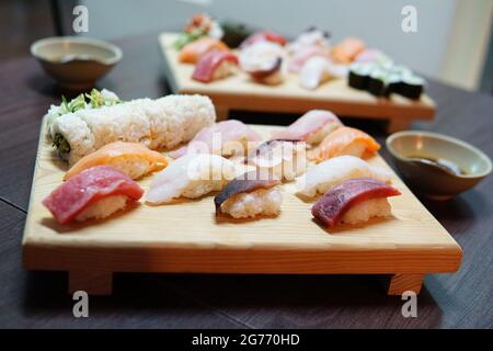 Zwei Portionen köstliches Sushi auf einem traditionellen Holzbrett mit Sojasauce Stockfoto
