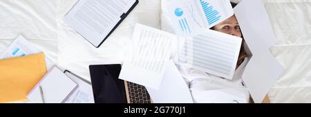 Müde Frau liegt auf dem Bett mit Laptop und Business-Charts Stockfoto
