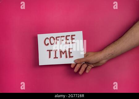 Nahaufnahme eines Mannes, der ein Papier mit dem Wort „COFFEE TIME“ auf einem fuchsienfarbenen Hintergrund hält Stockfoto