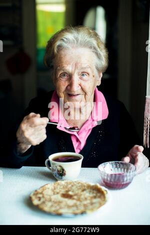 Eine alte Rentnerin trinkt zu Hause Tee mit Gebäck. Stockfoto