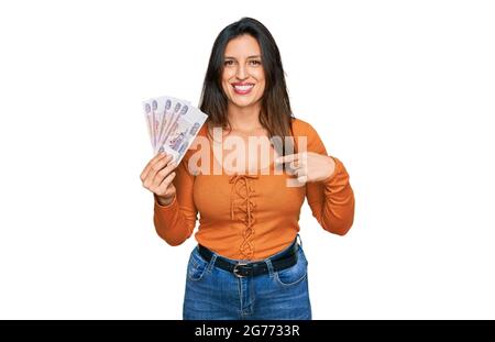 Schöne hispanische Frau mit russischen 500 Rubel-Banknoten, die mit dem Finger auf ein selbst lächelnd glücklich und stolz zeigen Stockfoto