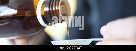 Der Mensch gießt Zuckersirup aus der Flasche in den Löffel Stockfoto