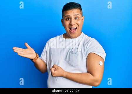 Junger lateinischer Mann, der die Taste des Blutzuckermessgeräts verwendet, feiert seine Leistung mit einem glücklichen Lächeln und mit erhobener Hand zum Ausdruck des Gewinners Stockfoto
