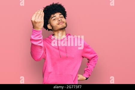 Junger afroamerikanischer Mann mit afro-Haaren trägt ein lässiges rosa Sweatshirt und tut italienische Geste mit Hand und Fingern selbstbewussten Ausdruck Stockfoto