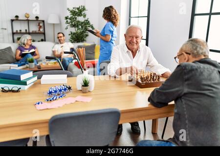 Zwei pensionierte Mann lächeln glücklich spielen Schach in Krankenschwester zu Hause. Stockfoto