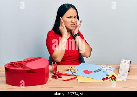 Schöne hispanische Frau mit Nasenpiercing tun Handwerk kreative Dekoration Abdeckung Ohren mit Fingern mit verärgerten Ausdruck für den Lärm von lo Stockfoto