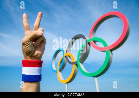 RIO DE JANEIRO - CA. MAI 2016: Eine Hand mit rot-weißem und blauem Armband macht vor den Olympischen Ringen ein Siegeszeichen Stockfoto