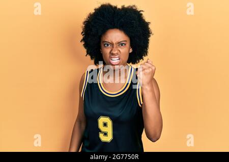 Junge afroamerikanische Frau trägt Basketballuniform wütend und verrückt Erhöhung der Faust frustriert und wütend, während schreiend vor Wut. Wut und Aggressi Stockfoto