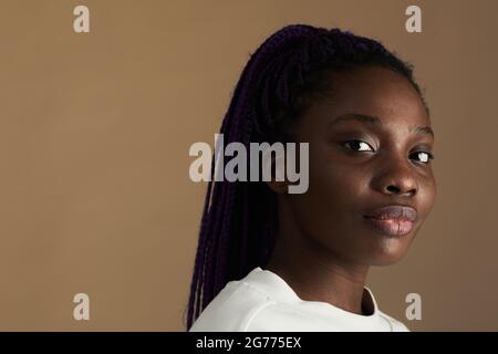 Minimales Nahaufnahme-Porträt einer jungen afroamerikanischen Frau, die vor beigefarbenem Hintergrund auf die Kamera schaut, Kopierraum Stockfoto