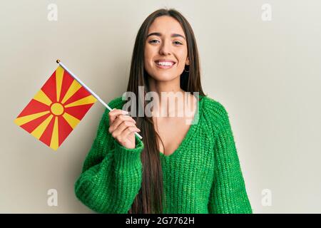 Junge hispanische Mädchen hält mazedonische Flagge positiv und glücklich stehend und lächelt mit einem selbstbewussten Lächeln zeigt Zähne Stockfoto