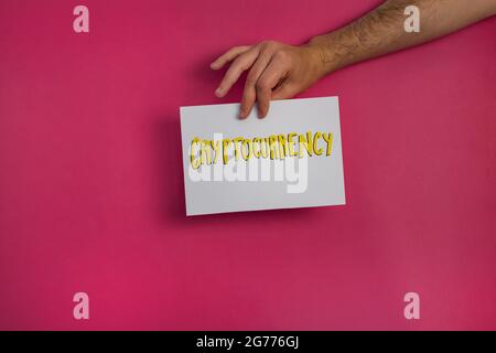 Eine Nahaufnahme eines Mannes, der ein Papier mit dem Wort „KRYPTOWÄHRUNG“ auf einem fuchsiafarbenen Hintergrund hält Stockfoto