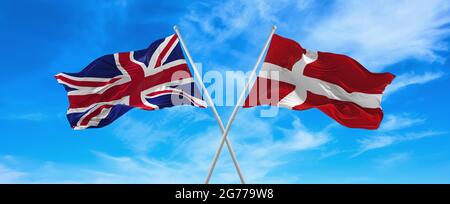 Flaggen von Großbritannien und dänemark winken im Wind auf Fahnenmasten gegen den Himmel mit Wolken am sonnigen Tag. Symbolisieren Beziehung, Dialog zwischen zwei Stockfoto