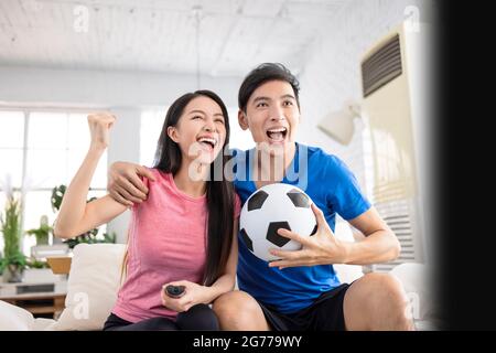 Aufgeregt Junges Paar Fernsehen und die Hände heben, um den Sieg zu feiern Stockfoto