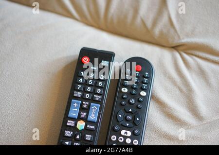 Zwei schwarze Kunststoff-Fernbedienungen auf dem Sofa Stockfoto