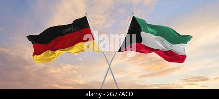 Flaggen von Deutschland und Kuwait winken im Wind auf Fahnenmasten gegen den Himmel mit Wolken am sonnigen Tag. Symbolisieren Beziehung, Dialog zwischen zwei Countris Stockfoto