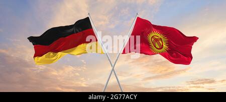 Flaggen von Deutschland und Kirgisistan winken im Wind auf Fahnenmasten gegen den Himmel mit Wolken am sonnigen Tag. Symbolisieren Beziehung, Dialog zwischen zwei Cou Stockfoto