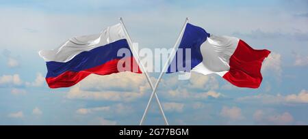 Flaggen von Russland und Frankreich winken im Wind auf Fahnenmasten gegen den Himmel mit Wolken am sonnigen Tag. Symbolisieren Beziehung, Dialog zwischen zwei Ländern Stockfoto