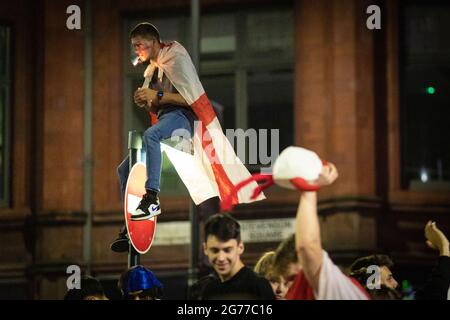 Manchester, Großbritannien. Juli 2021. Ein Mann zündet eine Zigarette an und saß nach dem Finale der Euro2020 auf einem Straßenschild. Unabhängig davon, dass sie beim Finale der Euro2020 gegen Italien verloren haben, feiern England-Fans nach dem Spiel auf dem Stevenson Square. Kredit: Andy Barton/Alamy Live Nachrichten Stockfoto