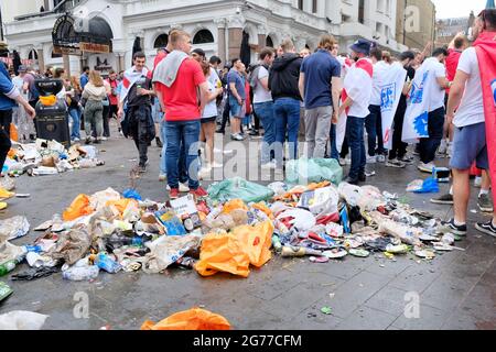 Englische Fußballfans wandern durch den Müll, der auf dem Leicester Square hinterlassen wurde, nachdem sich Hunderte vor dem Finale der Euro 2020 versammelt hatten. Stockfoto