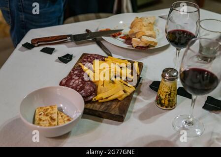 Tisch mit verschiedenen typisch italienischen Vorspeisen, Aufschnitt und Messer, auf einem rustikalen Holztisch. Gläser mit Rotwein. Selektiver Fokus. Stockfoto