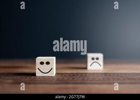 Fröhliche und traurige lächelnde Gesichter auf Holzblöcken. Konzept der Kundenzufriedenheit oder Bewertung Stockfoto