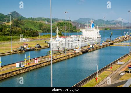 Eine große Ladung fuhr gerade an einem sonnigen Tag durch den Panamakanal. Die Hauptbüros und eine der Schleusen sind zu sehen. Stockfoto