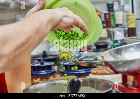 Der Koch stellt grüne Erbsen in eine Schüssel, um Backwaren mit Spargel und Erbsen zu machen. Schritt für Schritt Rezept Stockfoto