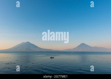 Atitlan See mit Toliman, San Pedro und Atitlan Vulkan bei Sonnenaufgang und Fischer, Panajachel, Guatemala. Stockfoto