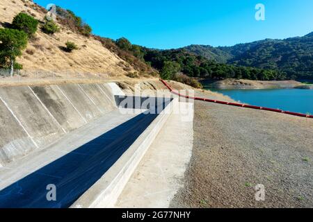 Betonstaudamm verschüttete, orangefarbener Schutt boomt auf trockenem Boden. Extrem niedriger Wasserstand bei der Trocknung im Sommer Stevens Creek Reservoir in San Francisco Ba Stockfoto