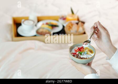 Hände einer jungen Frau, die Müsli mit frischem Joghurt, Beeren und Früchten zum Frühstück isst Stockfoto