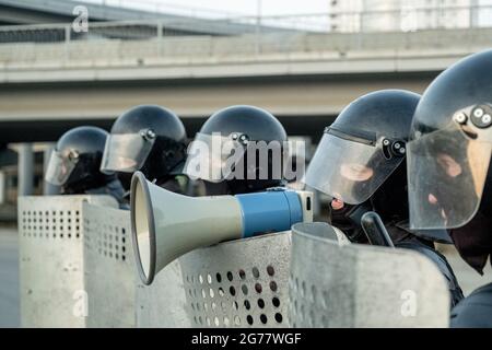 Polizist im Sturzhelm, der zwischen Mitarbeitern mit Schilden steht und in Mefaphon spricht, während er Terroristen neutralisiert Stockfoto