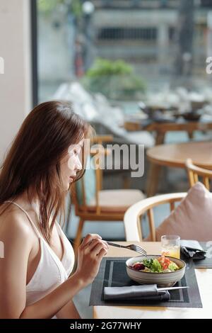 Hübsche junge Frau, die köstlichen Salat zum Mittagessen im Café genießt Stockfoto