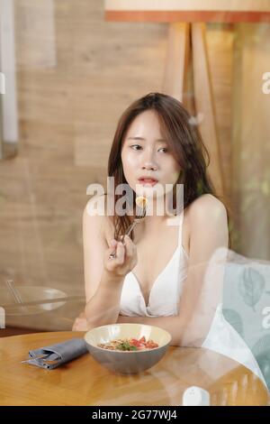 Porträt einer hübschen jungen Frau, die zum Frühstück Müsli mit Bananen- und Erdbeerscheiben isst Stockfoto