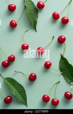 Flache Kirschbeeren und Blätter auf pastellgrünem Hintergrund legen. Draufsicht reife rote Kirschen auf dem Tisch Stockfoto