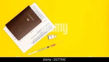 Covid-19 geimpfte Ausweispapiere und Reisepass mit Coronavirus-Impfstoffflasche und -Spritze auf gelbem Hintergrund mit Kopierraum Stockfoto