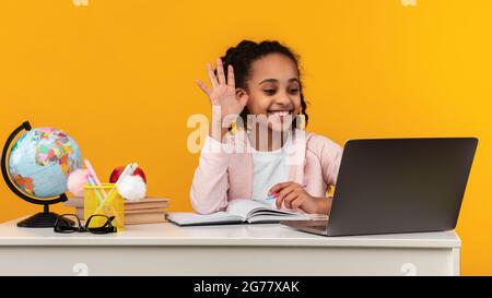 Portrait eines lächelnden schwarzen Mädchens, das am Tisch sitzt und winkt Stockfoto