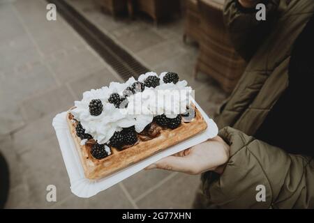 Detail der traditionellen polnischen Spezialität Gofry mit Schlagsahne und Brombeeren auf Frauenhand Stockfoto