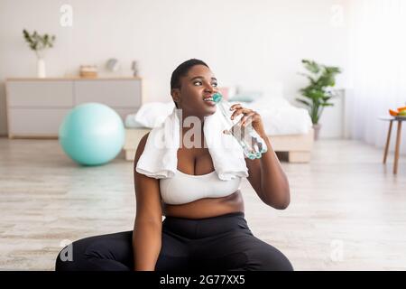 Wellness und Gewichtsverlust. Plus Größe schwarze Dame trinken frisches klares Wasser aus der Flasche nach dem Sport-Training zu Hause Stockfoto