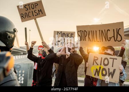 Eine Gruppe von wütenden Aktivisten, die in Masken mit Schilder und Sreaming auftraten, während sie an einer Kundgebung aus Protest gegen Rassismus teilnahmen Stockfoto