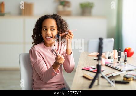 Beauty Blogging. Fröhliche afroamerikanische Teenager, die Kosmetik-Produktbewertung aufzeichnen, mit Telefon auf Stativ Stockfoto