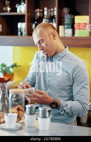 Der Barkeeper telefoniert mit dem Kunden, der die Lieferung bestellt, und schreibt die Bestelldetails auf Stockfoto