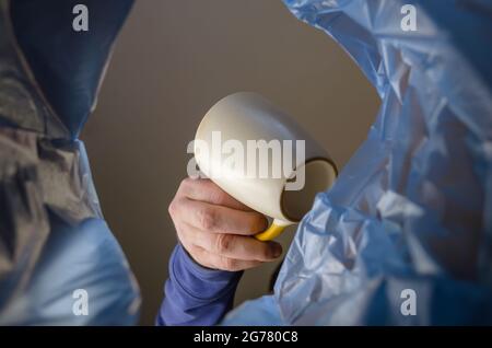 Mit der Hand wird ein Keramikbecher in einen Mülleimer geschmeißt. Der Mann hält einen leeren Becher über den Müllkorb. Ansicht von unten. In Innenräumen. Stockfoto