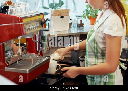 Nahaufnahme einer Barista-Frau, die frische Milch oder Rahm für den Gast in eine Tasse Kaffee gießt Stockfoto