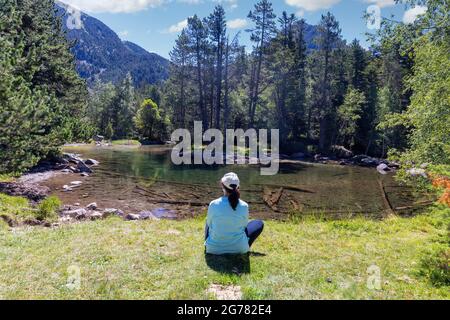 Schöne Berglandschaft der Pyrenäen, Sant Maurici und Augestortes, eine Frau, die in der Nähe des Sees sitzt, Spanien, Katalonien. Stockfoto