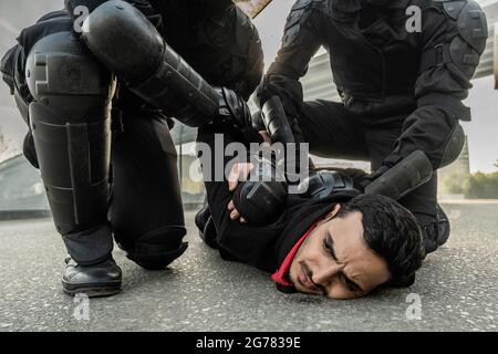 Krawallkraft in Schutzkleidung drückt den Mann aus dem Nahen Osten zu Boden, während er ihn während der Kundgebung festnahm Stockfoto